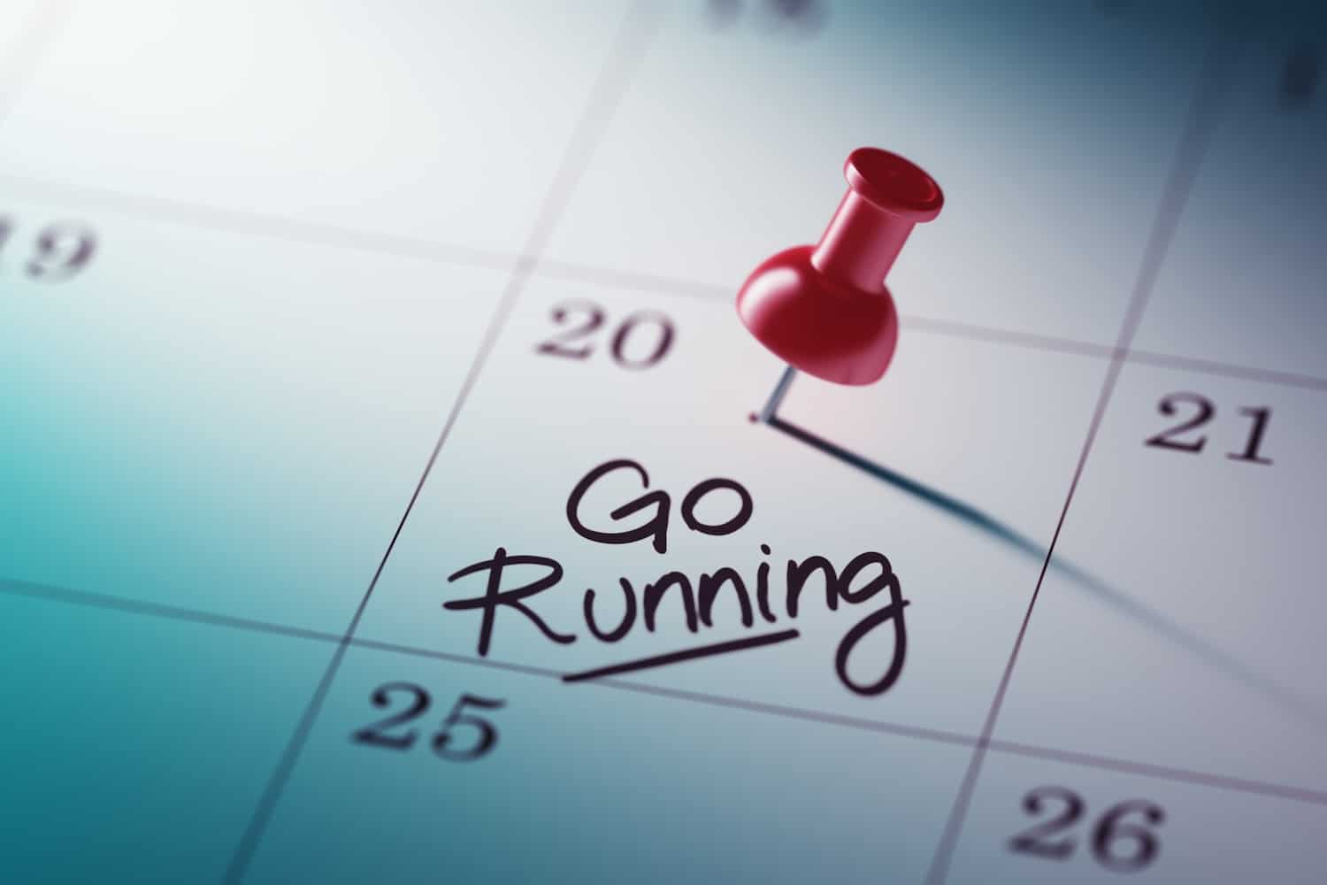 Calendar with a red push pin on a date with the he words "go running" written