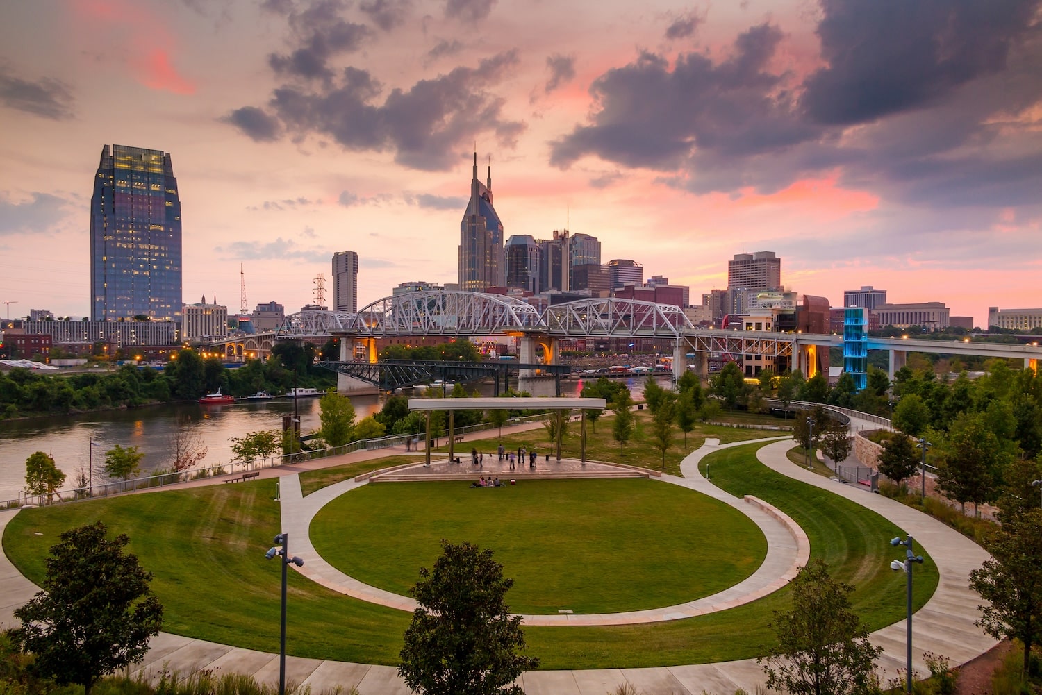 A park with sidewalks across the river from the Nashville downtown skyline